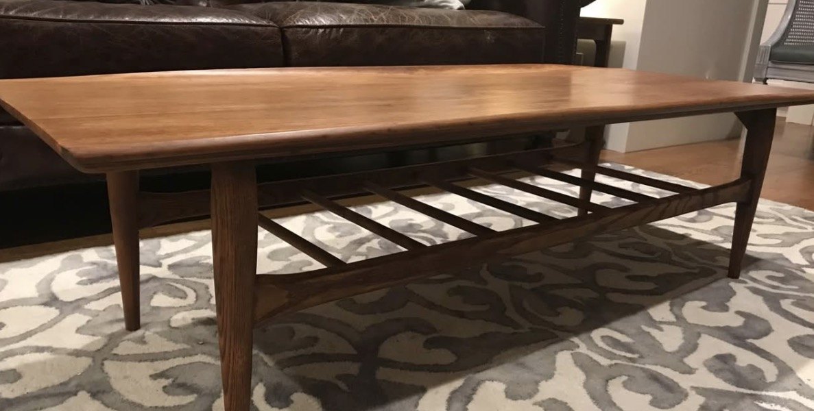 A refinished mid-century coffee table with a surfboard-shaped top, a slatted lower shelf and tapered legs